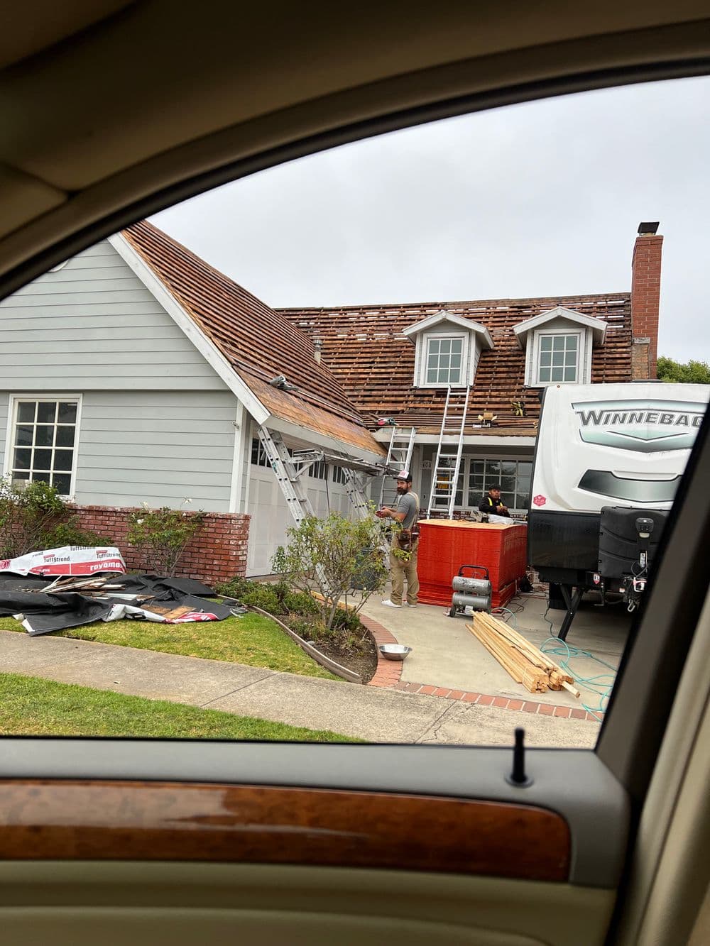 Roof renovation in progress on a house, with construction materials and a trailer in view.